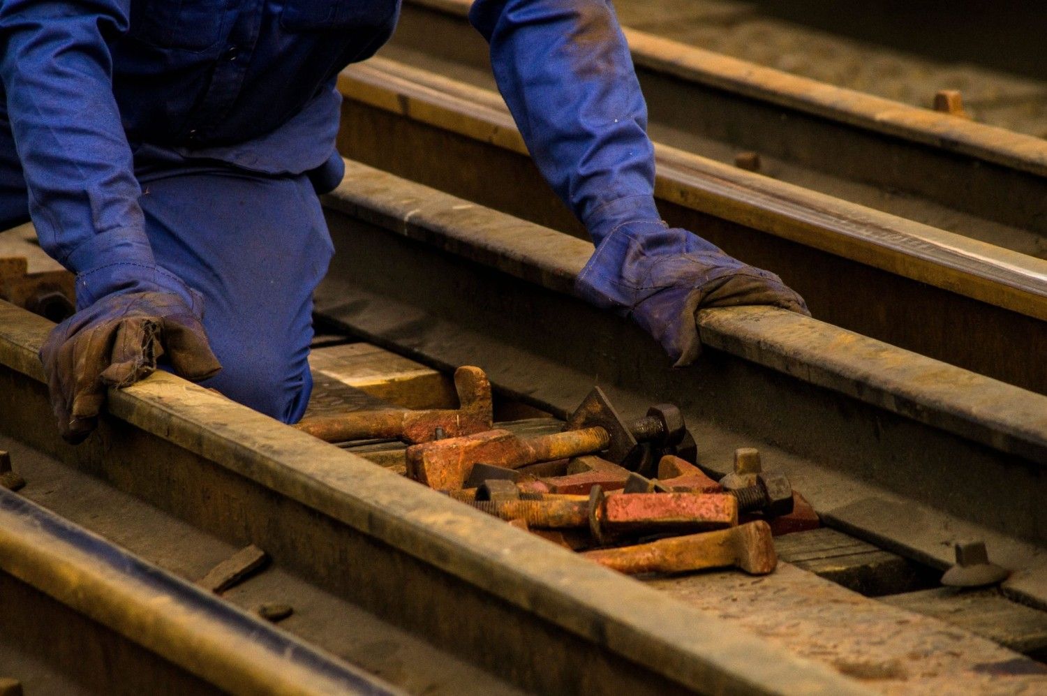 Nahaufnahme eines Arbeiters in Schutzkleidung, der Gleise mit Werkzeugen instand hält.